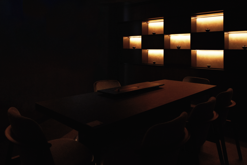 A private tea room with soft lighting highlighting tea vessels, creating a tranquil and intimate atmosphere for guests to relax and enjoy tea.