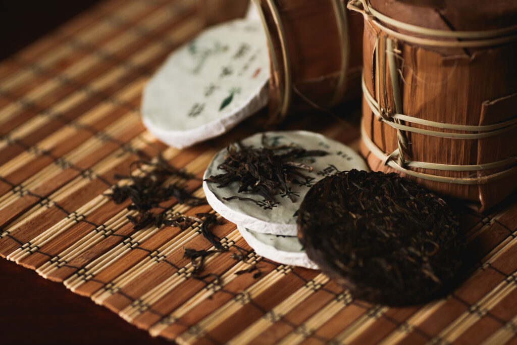 A stack of traditional compressed pu erh tea cakes is neatly arranged in bamboo storage, allowing for natural ventilation. The cakes, made from fermented tea leaves, showcase the unique textures and colors typical of high-quality pu erh tea, emphasizing their cultural significance in tea brewing.