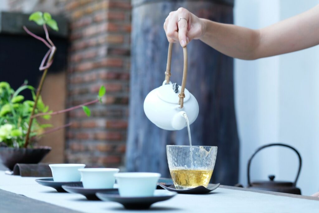 A traditional Chinese tea master is meticulously preparing green tea in an authentic ceremony setting, surrounded by elegant tea utensils and loose leaf tea leaves. The scene captures the rich cultural heritage of tea consumption, highlighting the health benefits associated with drinking green tea.
