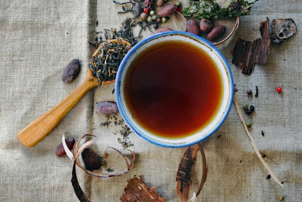 A warm cup of black tea beside a spoon filled with loose black tea leaves, capturing the aroma and purity of the brew