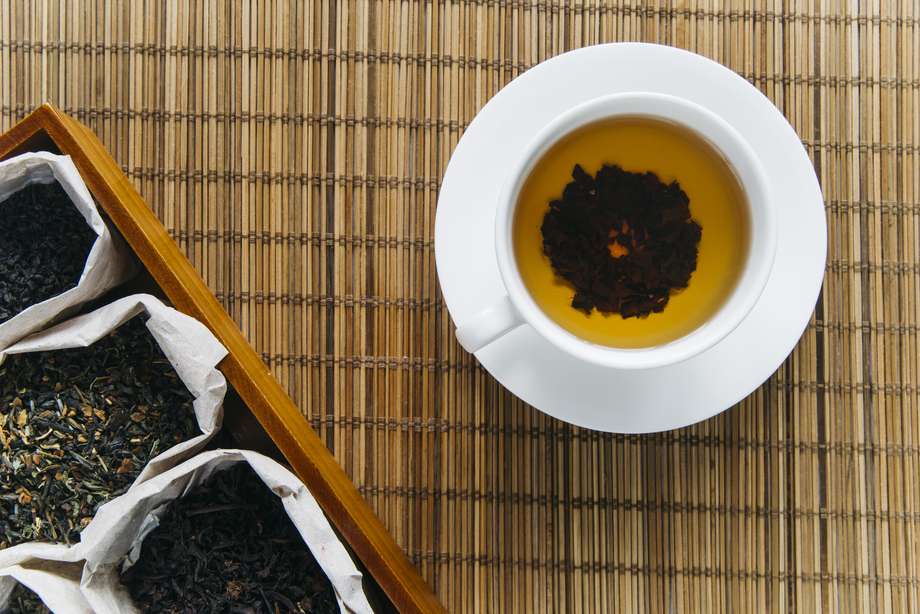 pu erh tea caffeine : A warm cup of pu erh tea beside loose tea leaves on the table, highlighting its deep colour and earthy aroma.