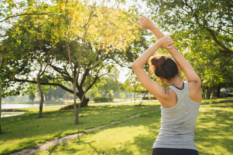 A healthy woman doing exercises at a park surrounded by greenery, representing vitality and mindfulness
