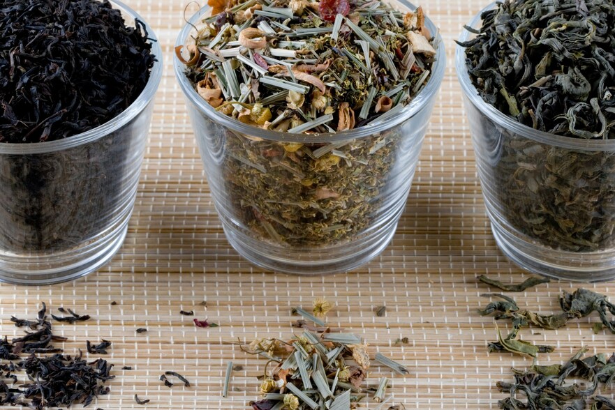Three varieties of loose-leaf tea displayed on a wooden table, each showing different colours and textures