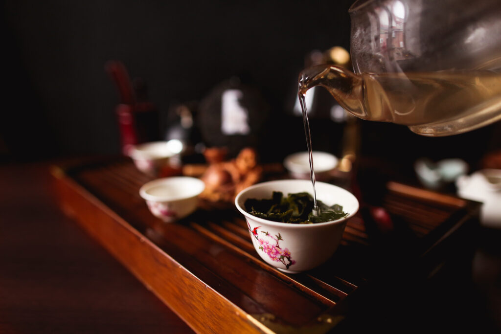 A close-up of hot tea being gently poured into a small porcelain teacup, with steam rising gracefully, capturing the tranquillity and precision of traditional tea serving