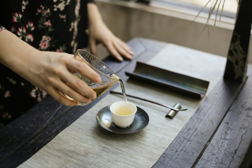 A steady hand pouring tea into a porcelain cup, capturing the graceful flow of liquid and the mindful precision of traditional tea preparation.