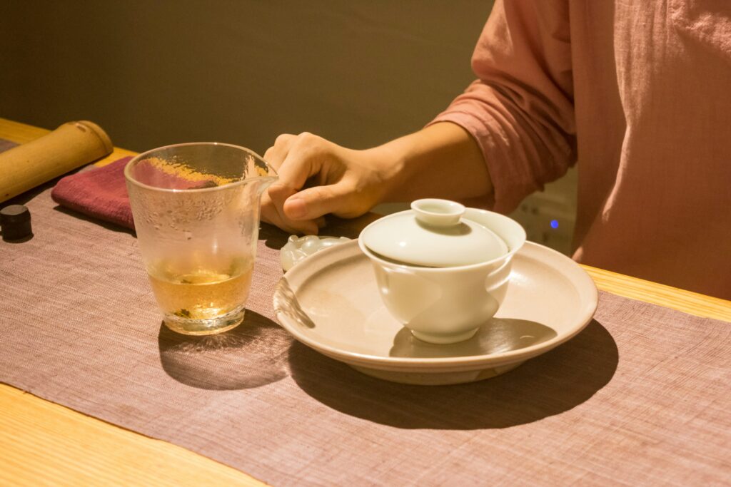 A tea master seated beside a table and a teacup with composed focus, reflecting tradition, expertise, and the quiet elegance of a tea ceremony.