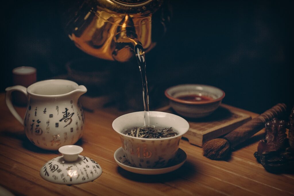 A traditional Chinese tea master is preparing Long Jing tea, also known as Dragon Well tea, in a tranquil West Lake setting, surrounded by lush tea plants. The scene captures the essence of Chinese tea culture, showcasing the meticulous process of brewing this premium green tea, celebrated for its many health benefits, including rich antioxidant content and support for heart health.