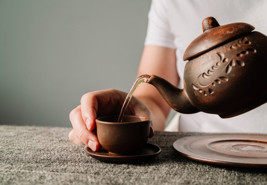 A hand gently pours hot tea from a traditional Chinese teapot into a small porcelain cup, capturing the calm, flowing motion of a classic tea ceremony.