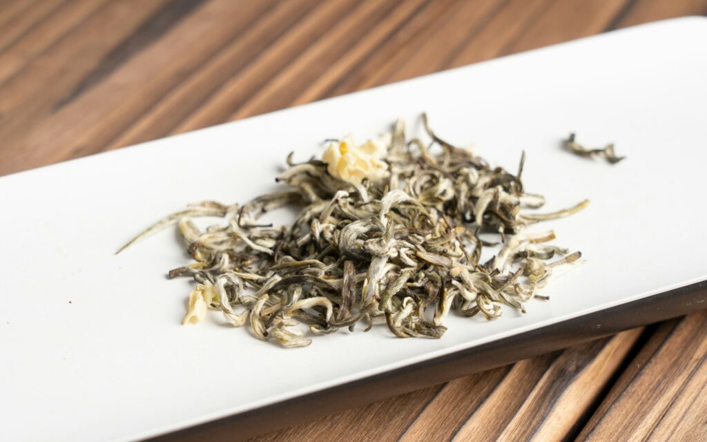 Carefully selected white tea leaves displayed on a ceramic plate, showcasing their natural silvery tones and fine texture, highlighting purity and craftsmanship.