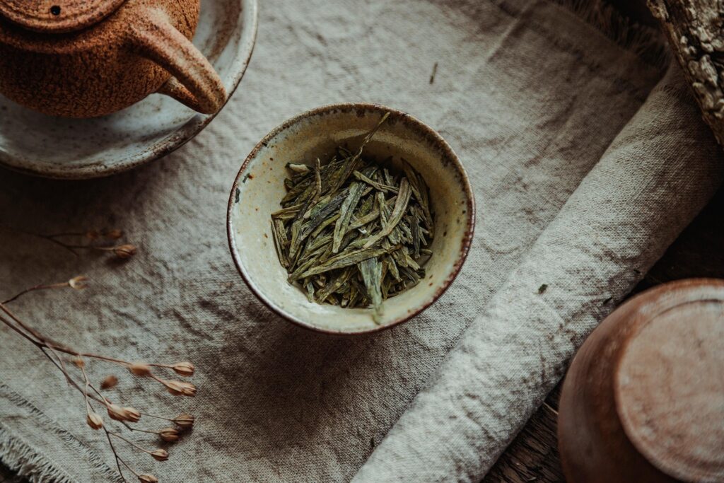 A close-up of Long Jing tea leaves resting in a porcelain cup, showcasing their flat emerald shape and delicate aroma, symbolising traditional Chinese tea craftsmanship.