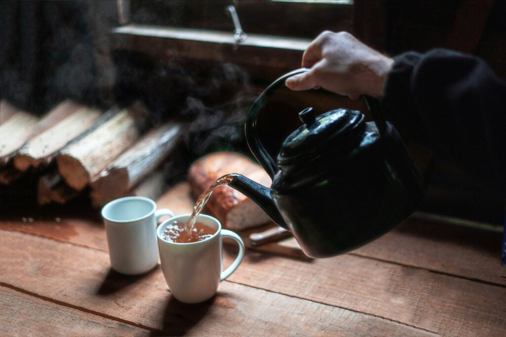 A hand gently tilting a teapot to pour black tea, emphasising elegance, craftsmanship, and the ritual of tea brewing.