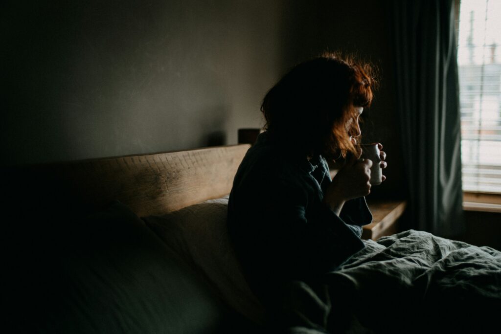 A woman enjoying a cup of tea while relaxing on her bed, creating a serene and intimate moment of comfort and mindfulness.