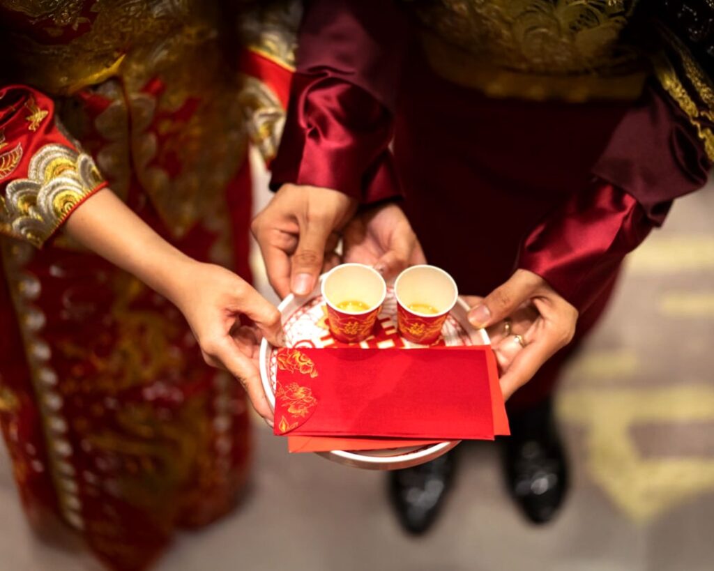 The bride and groom’s hands holding tea cups alongside angpao, symbolising blessings, respect, and prosperity.
