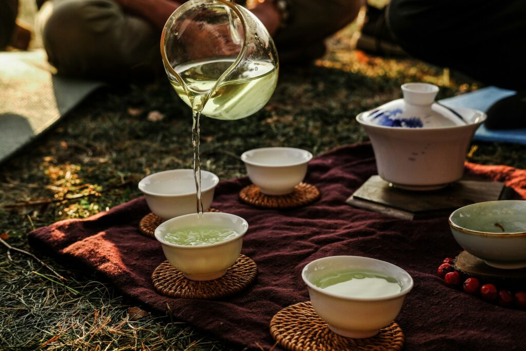 A hand slowly pouring green tea into small tea cups, reflecting the elegance and mindfulness of traditional tea-serving rituals.