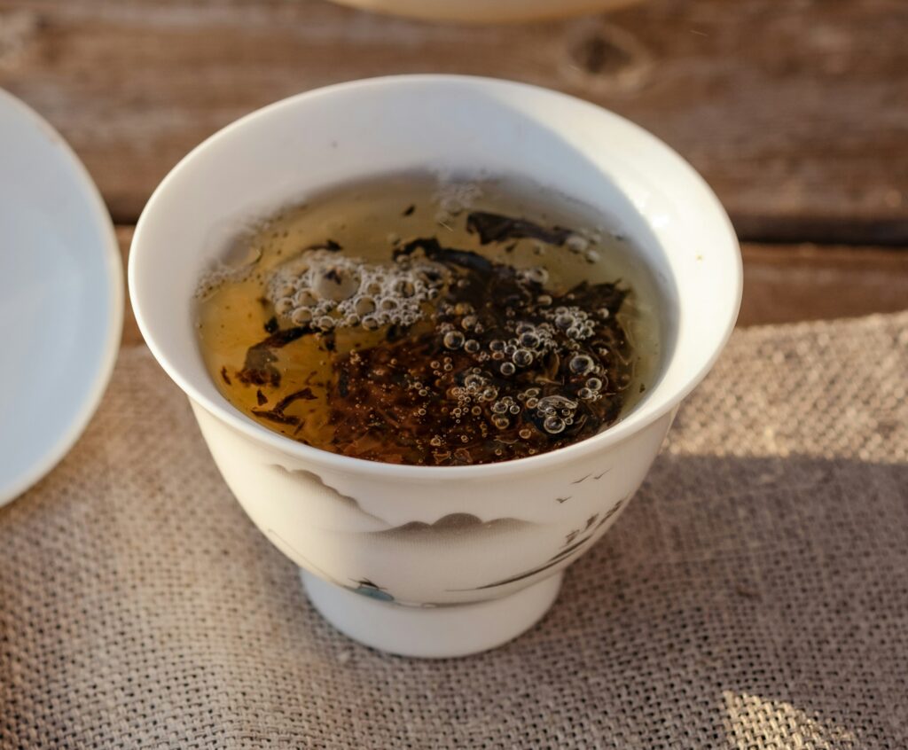 Dark Pu-erh tea leaves unfurling gently in hot water inside a tea cup, releasing earthy aromas and rich depth as the infusion slowly develops.