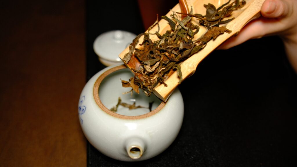 A close-up of hands gently pouring brewed tea leaves into delicate tea cups, capturing the calm ritual and precision of traditional tea preparation.