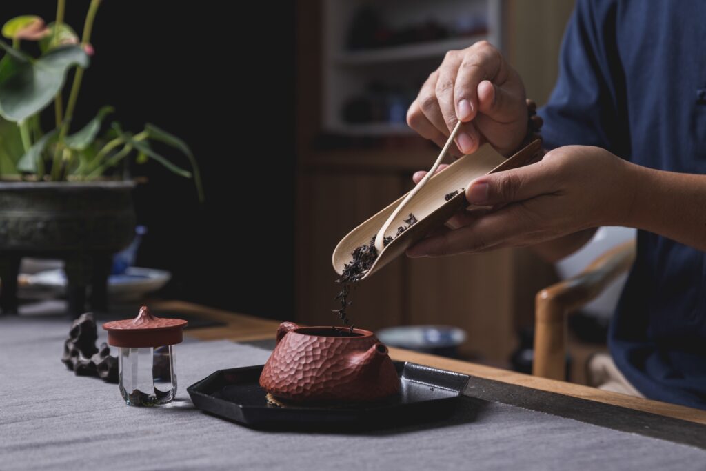 A man gently pours premium dry tea leaves into a traditional teapot, marking the beginning of a mindful tea preparation ritual.