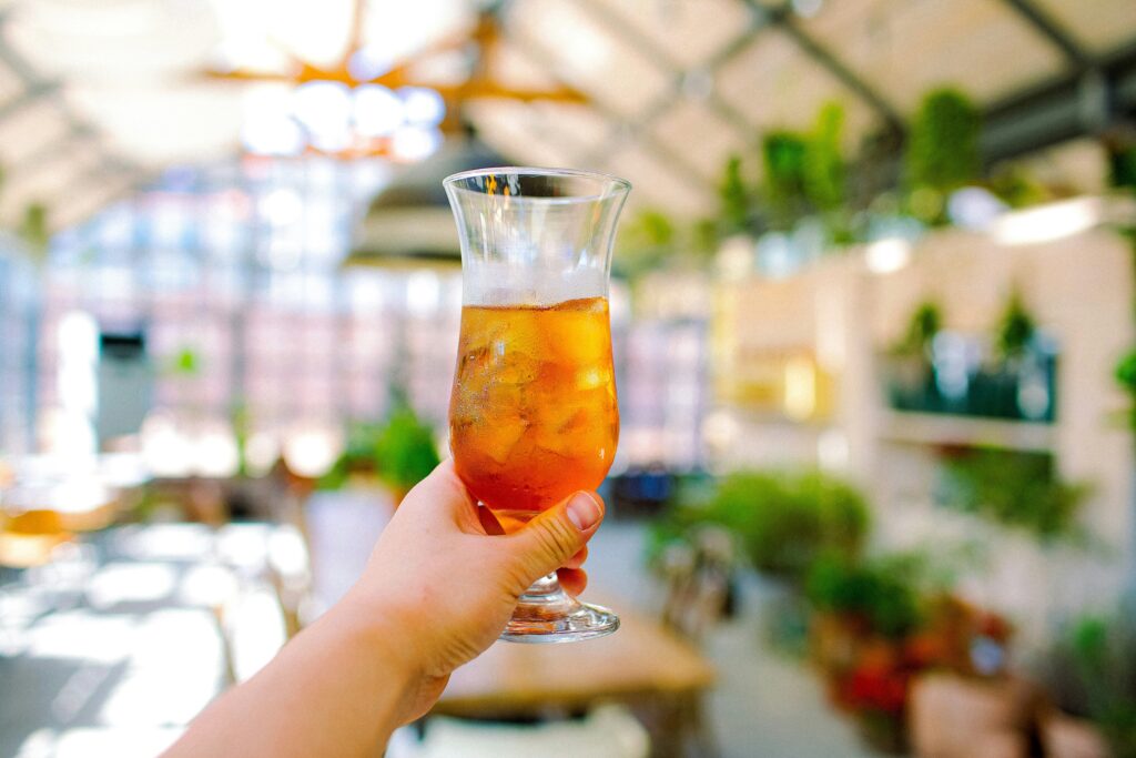 A hand holding a glass of iced tea, captured in natural light, conveying refreshment and modern tea enjoyment in a casual, everyday setting