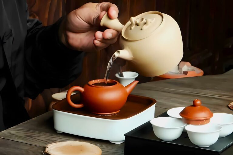 A person pours hot water from a beige teapot into a small clay teapot on a wooden tray, surrounded by white teacups, creating a calm and traditional tea-making scene.