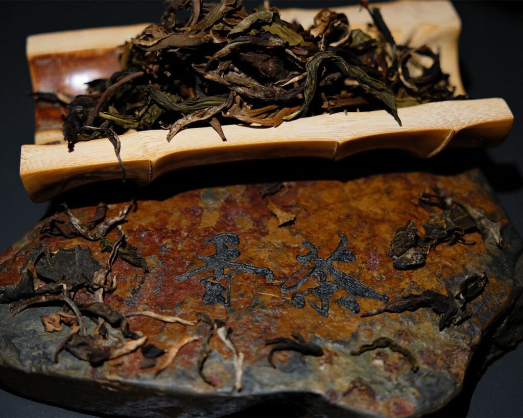 Dry tea leaves resting on a textured rock surface, highlighting their natural shape and earthy colour in a calm, minimalist setting.