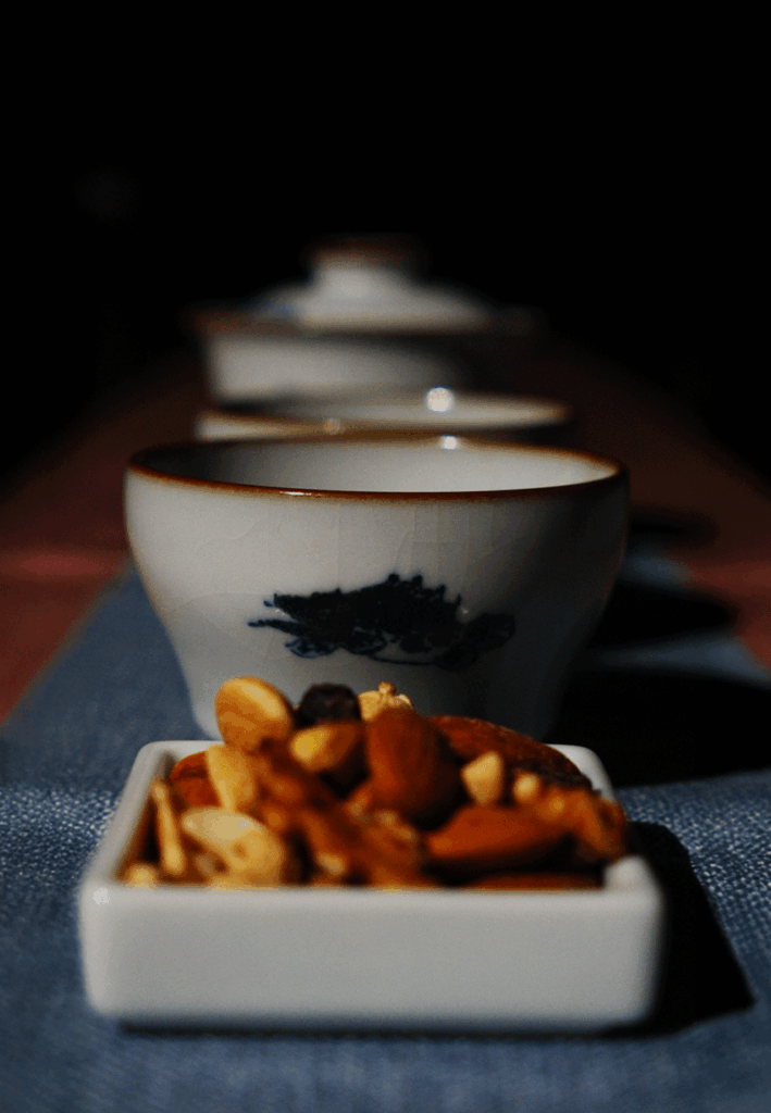 A Chinese teacup sits beside a small plate of nuts, presenting a balanced pairing of warm tea and light traditional snacks.