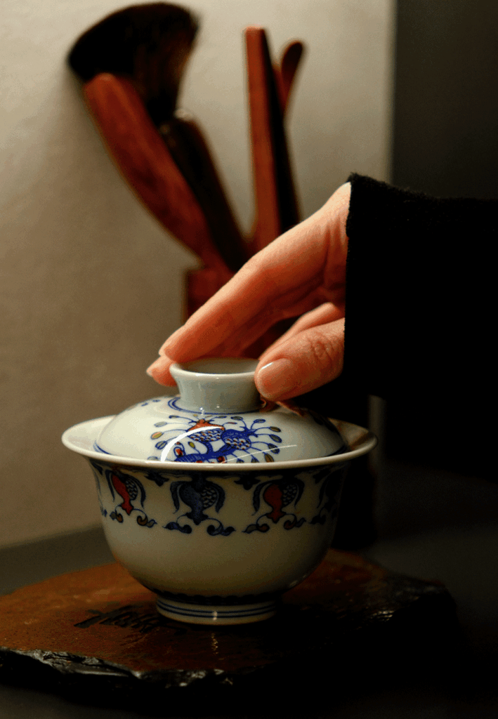 A hand lifts a Chinese teacup carefully, suggesting appreciation for the tea’s warmth and the craftsmanship of the cup.