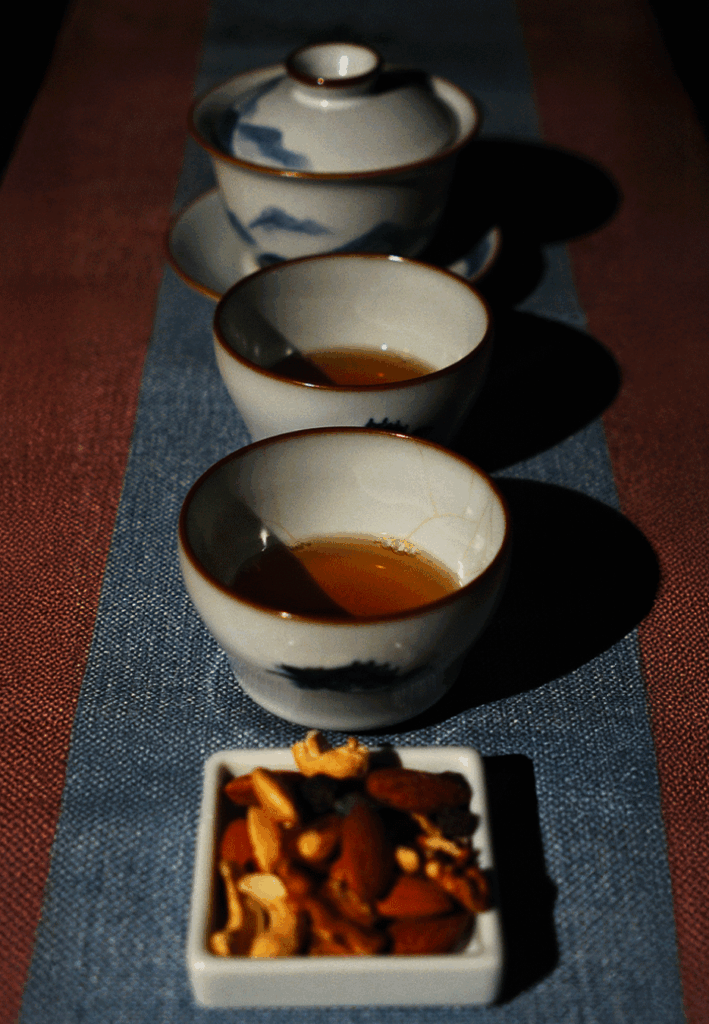 A teacup filled with freshly brewed tea is placed next to a plate of nuts, evoking a quiet and mindful tea moment.