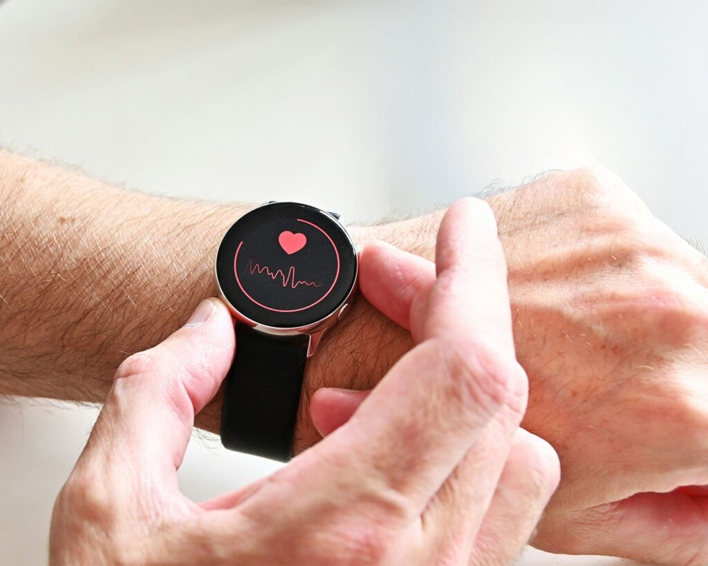 A hand resting near a smartwatch that displays a heart rate reading, symbolising self-awareness, health monitoring, and a quiet pause to check one’s body condition.