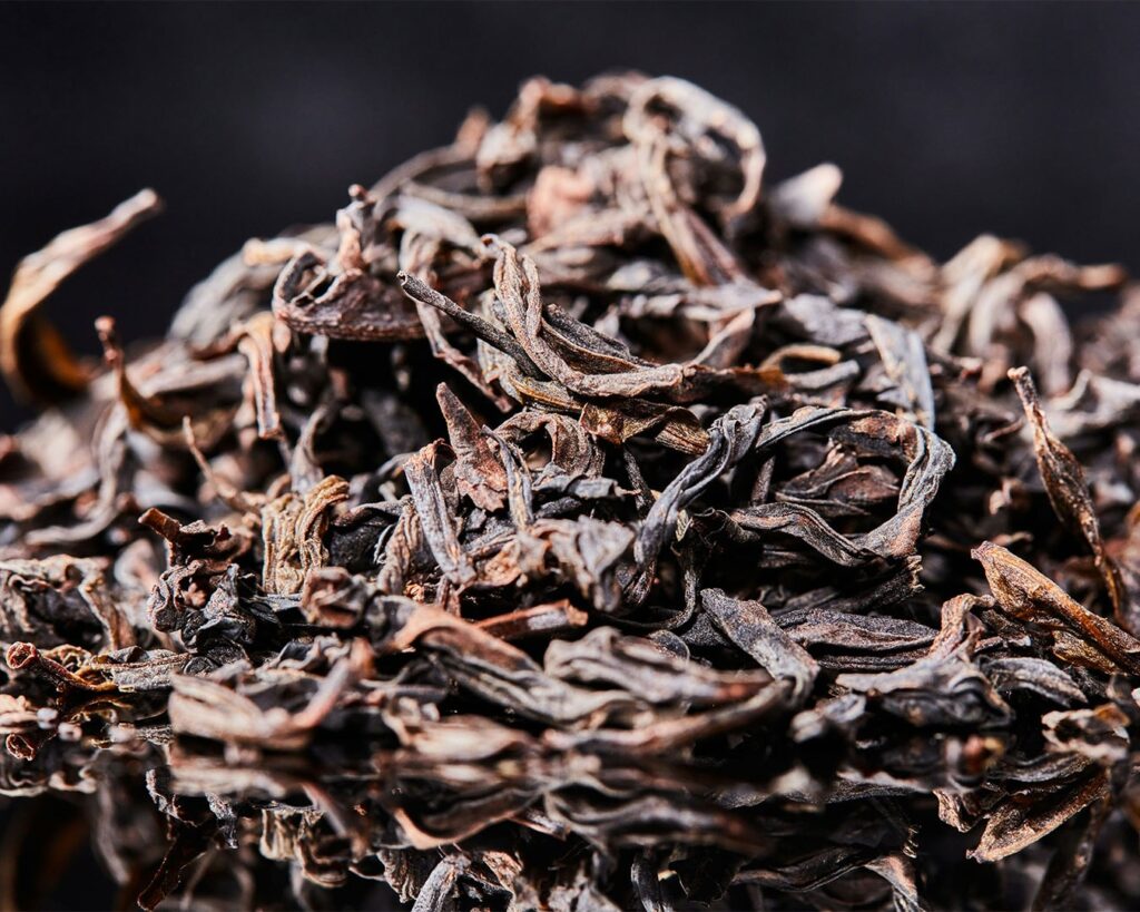 Dried loose tea leaves resting in a ceramic dish, showing natural shape and texture before brewing.
