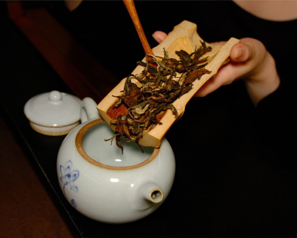 A hand gently placing tea leaves into a teapot, capturing the careful and mindful preparation process of Chinese tea brewing.