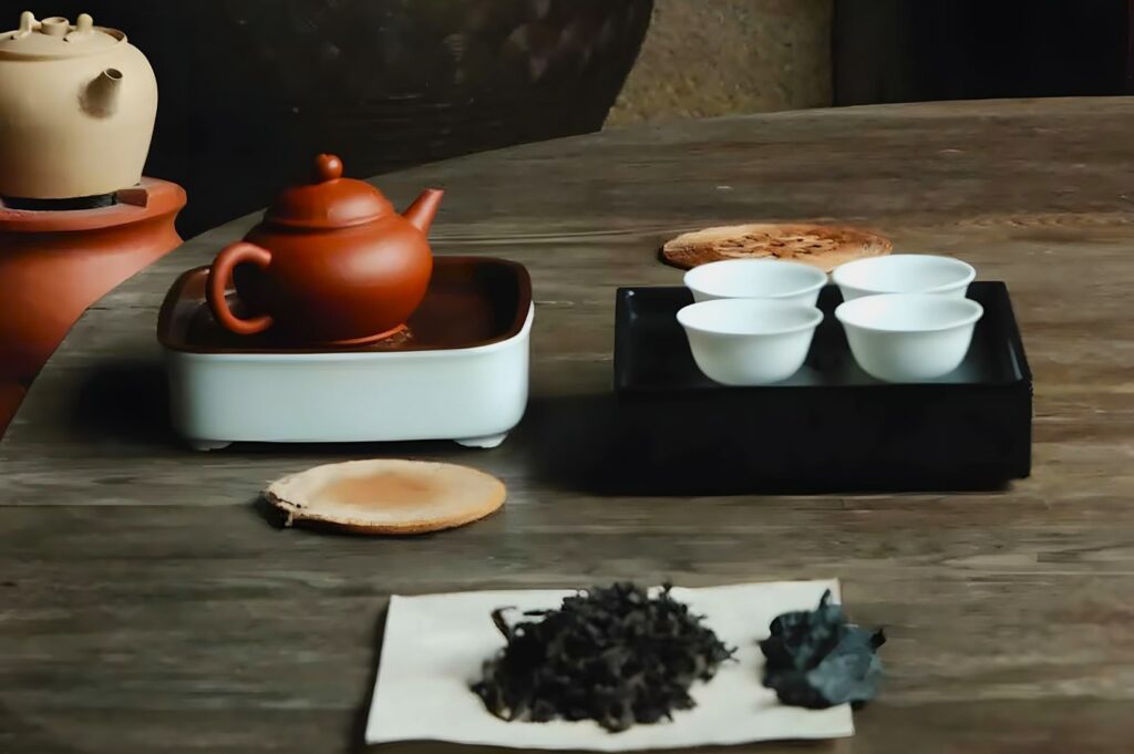 A rustic tea set on a wooden table includes a brown teapot, three small white cups, and loose tea leaves on paper, evoking a calm, traditional ambiance.