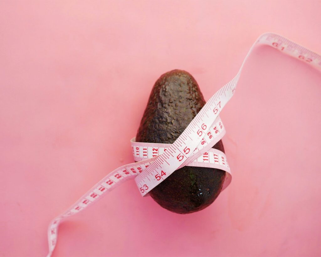 A measuring tape wrapped around an avocado, representing healthy eating, weight management, and a balanced lifestyle.
