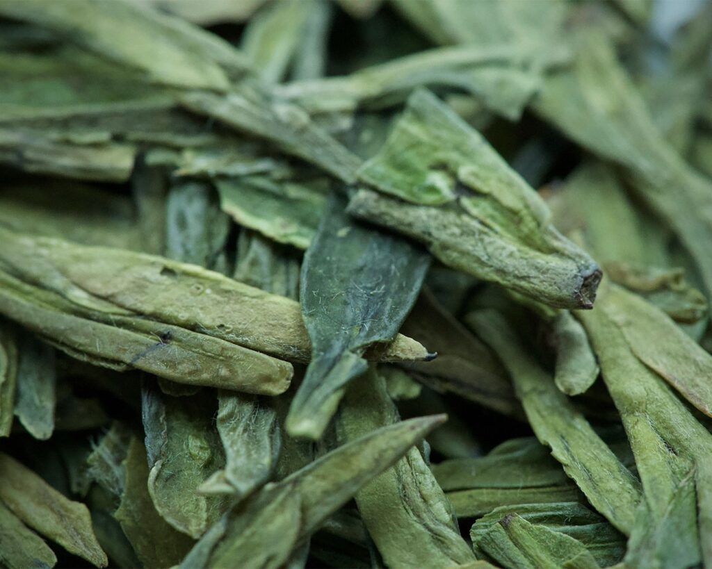 Close-up of fresh Longjing tea leaves, showing their flat shape and soft green colour, highlighting the natural texture and quality of this famous Chinese green tea.