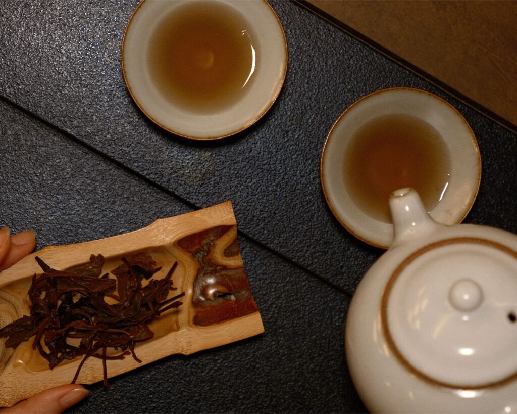 A ceramic tea cup and teapot set arranged beside fresh tea leaves, highlighting the harmony between tea ware and natural ingredients.