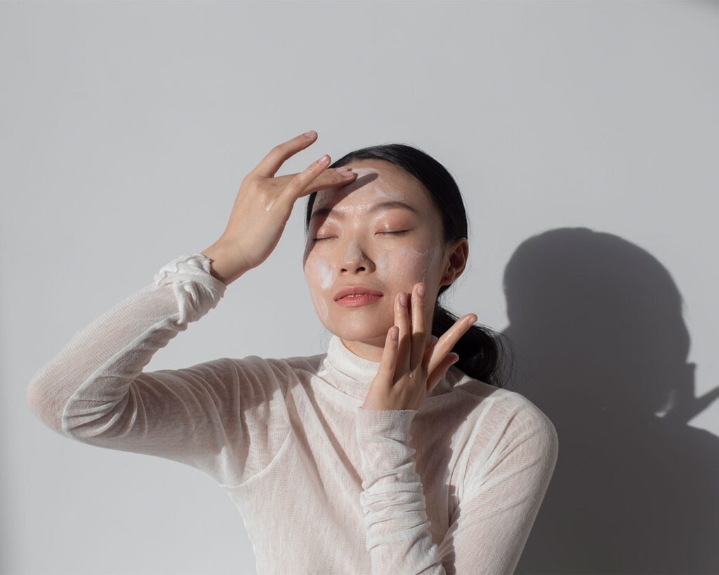 A woman gently touching her face with a calm expression, suggesting skincare, youthfulness, and anti-ageing beauty care.