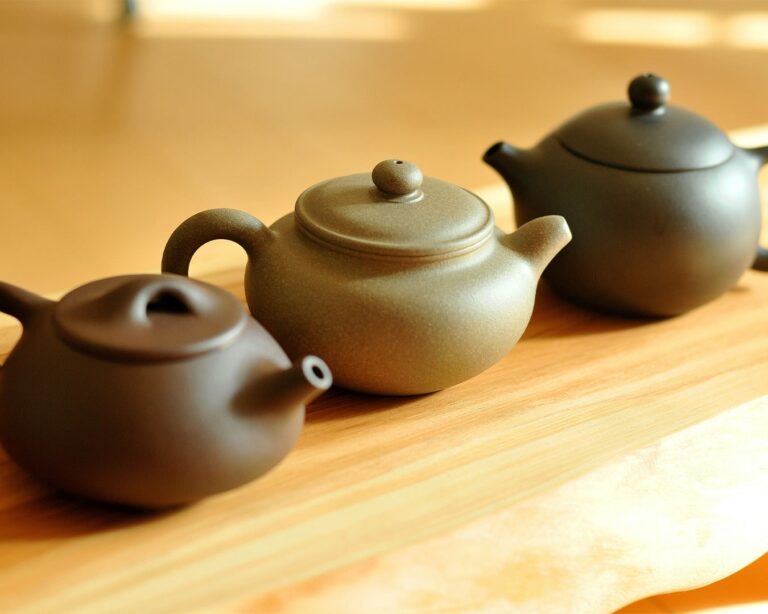 Handcrafted Yixing clay teapots displayed in warm light, known for enhancing tea flavour through natural porous clay.