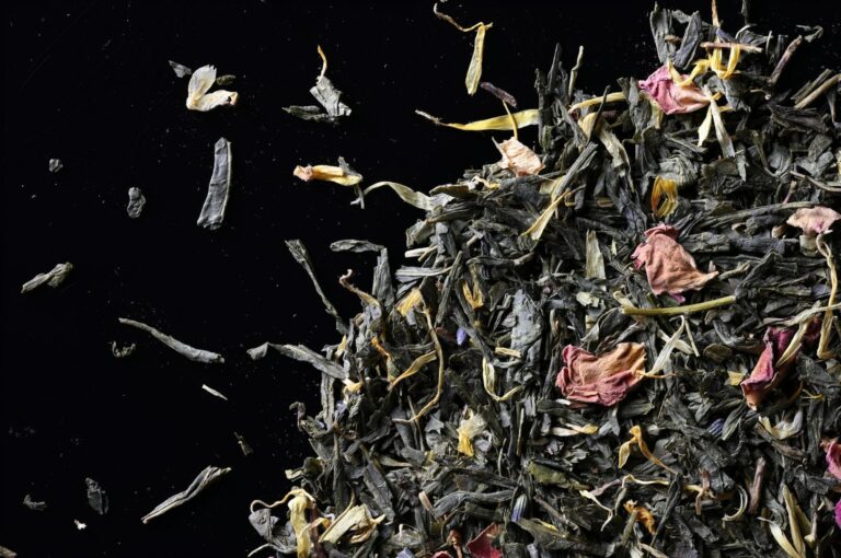 A close-up of loose-leaf green tea mixed with dried flower petals on a black background, showcasing a textured and colorful blend.