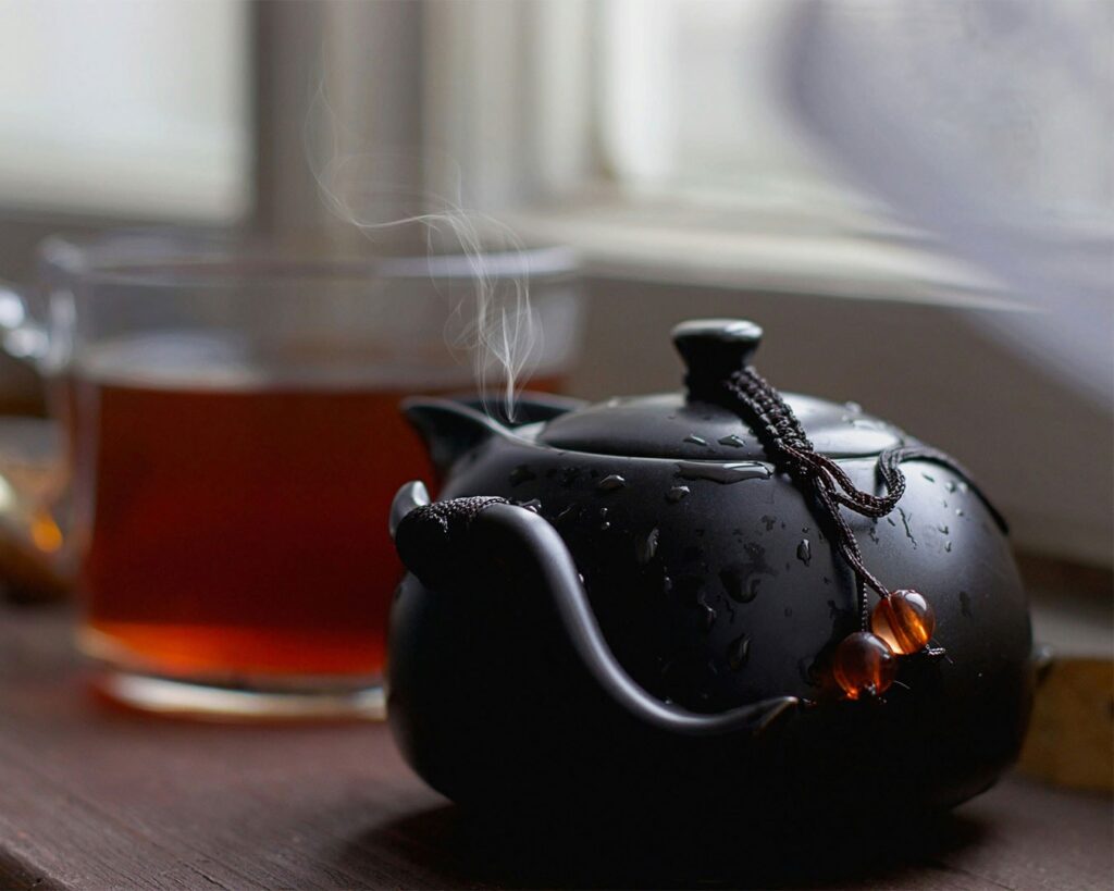 Tea leaves steeping inside a teapot with visible steam, capturing the brewing process and the soothing atmosphere of a freshly prepared cup of tea.