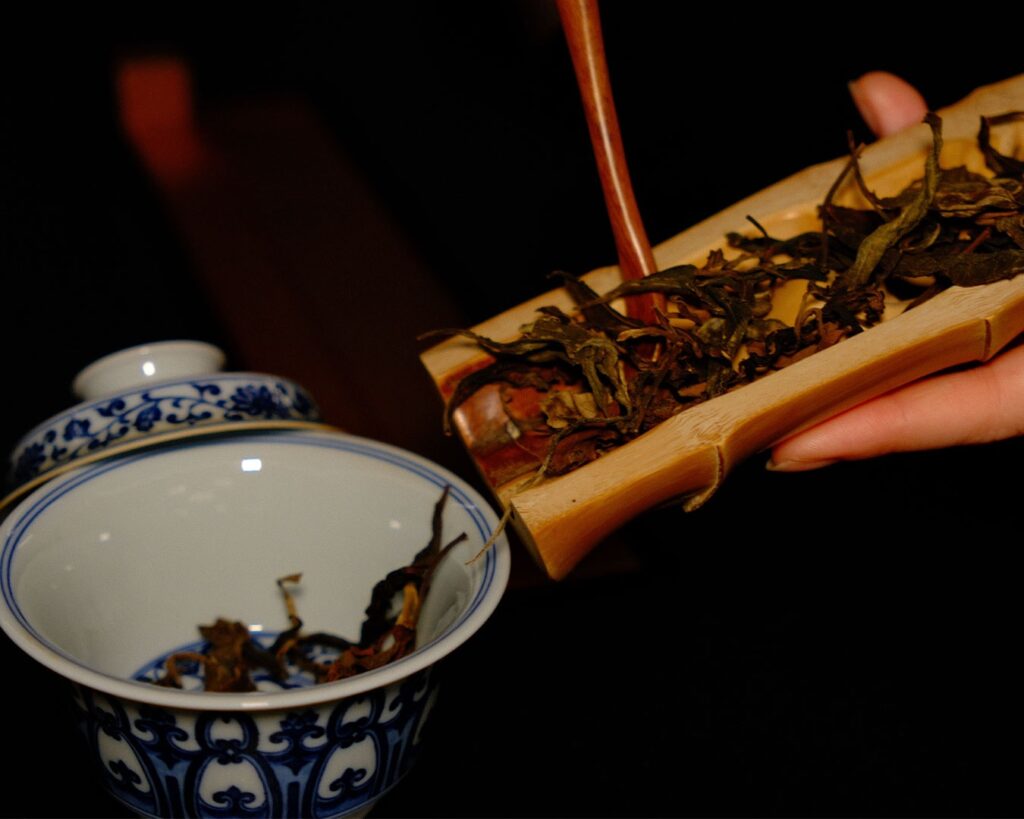 A hand gently releasing tea leaves into a cup, capturing the intimate ritual of tea brewing and the moment where aroma and tradition begin.