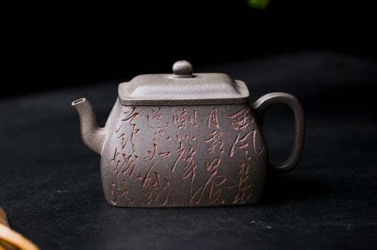 Square, dark gray teapot with Chinese calligraphy engraved on its surface, placed on a black background. The design feels elegant and traditional.