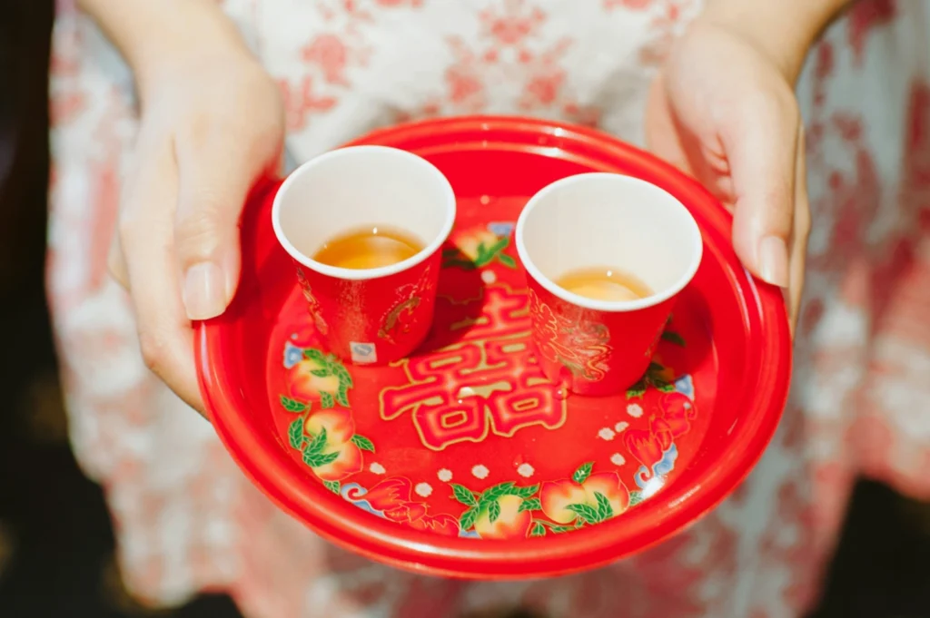 Hands hold a red tray with Chinese tea cups. The tray features festive symbols and designs, conveying a sense of tradition and celebration.