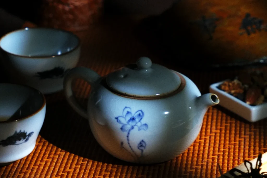 A serene scene with a white teapot and cups, adorned with blue floral designs, resting on a woven mat. Gentle light creates a peaceful ambiance.