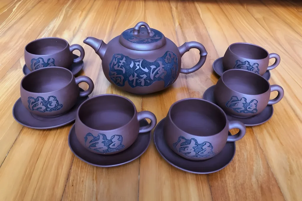 A brown clay tea set with one teapot and six cups with saucers, each adorned with intricate blue patterns. Set on a wooden surface.
