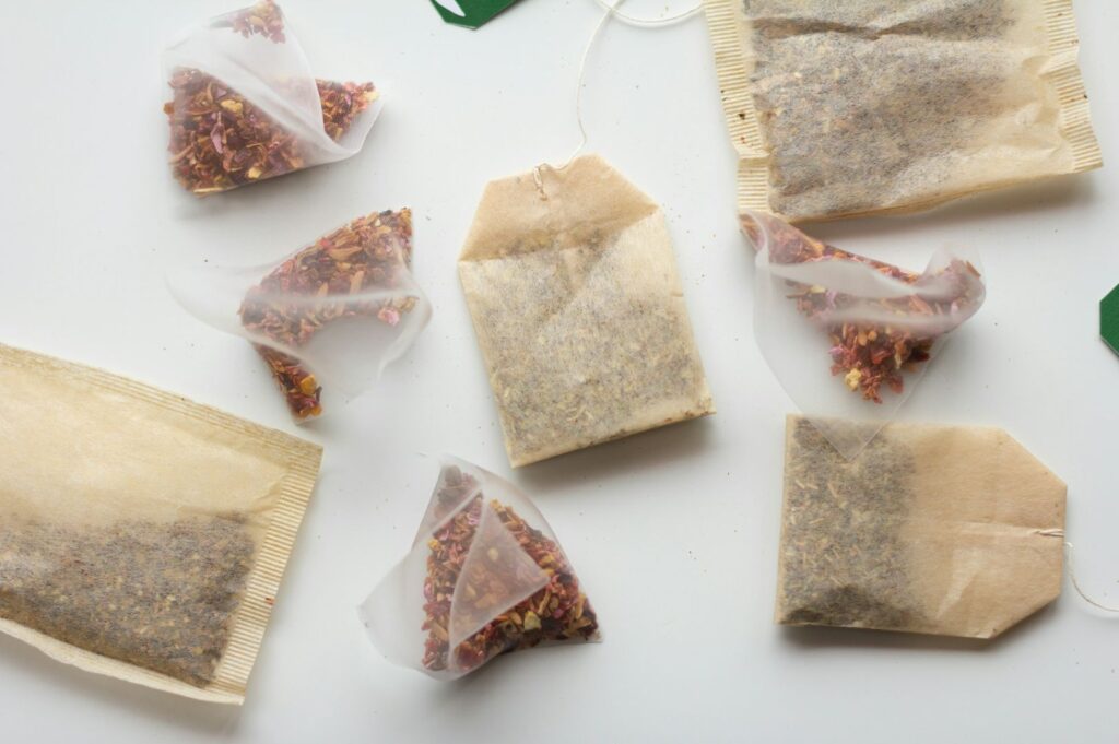 A flat lay of tea bags and transparent sachets on a light background, exposing colorful dried herbs and petals inside each pouch.