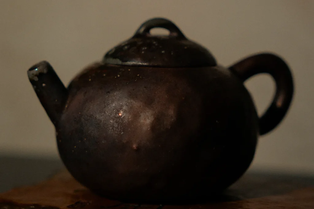 A worn, dark brown teapot with a round body and sturdy handle rests on a wooden surface, evoking a nostalgic and rustic atmosphere.