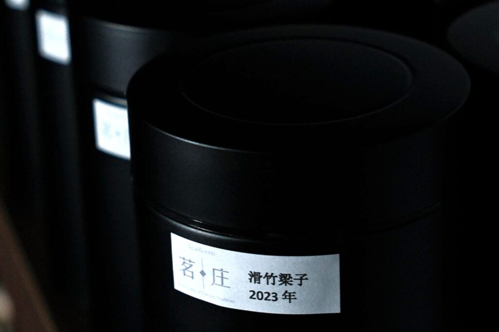 Close-up of black cylindrical containers with white labels in Japanese, dated 2023. The arrangement conveys a minimalist, organized aesthetic.