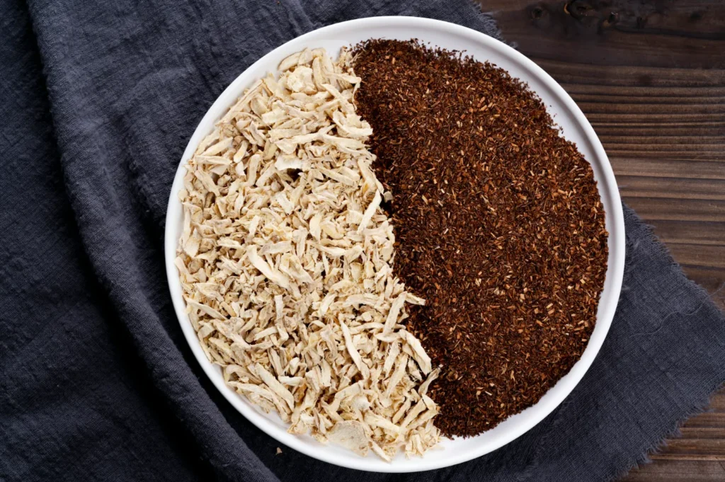 A white plate on a dark cloth background holds two ingredients; shredded, beige dried roots on one side and finely ground, dark brown powder on the other.