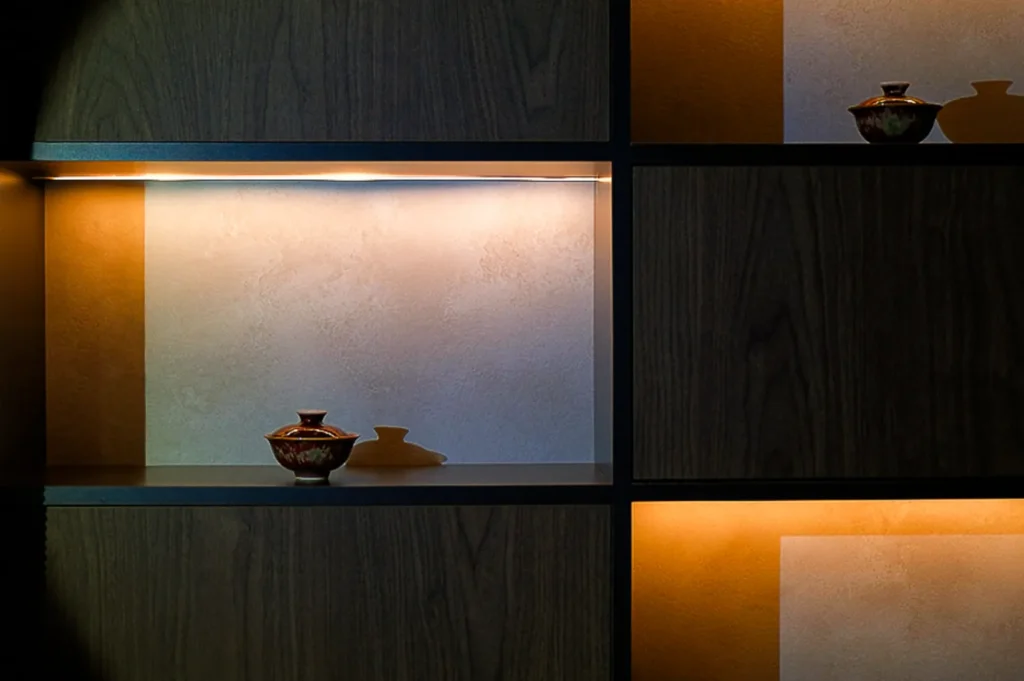 Minimalist shelves with soft lighting showcase small decorative vases. Warm tones and shadows create a cozy and elegant atmosphere.