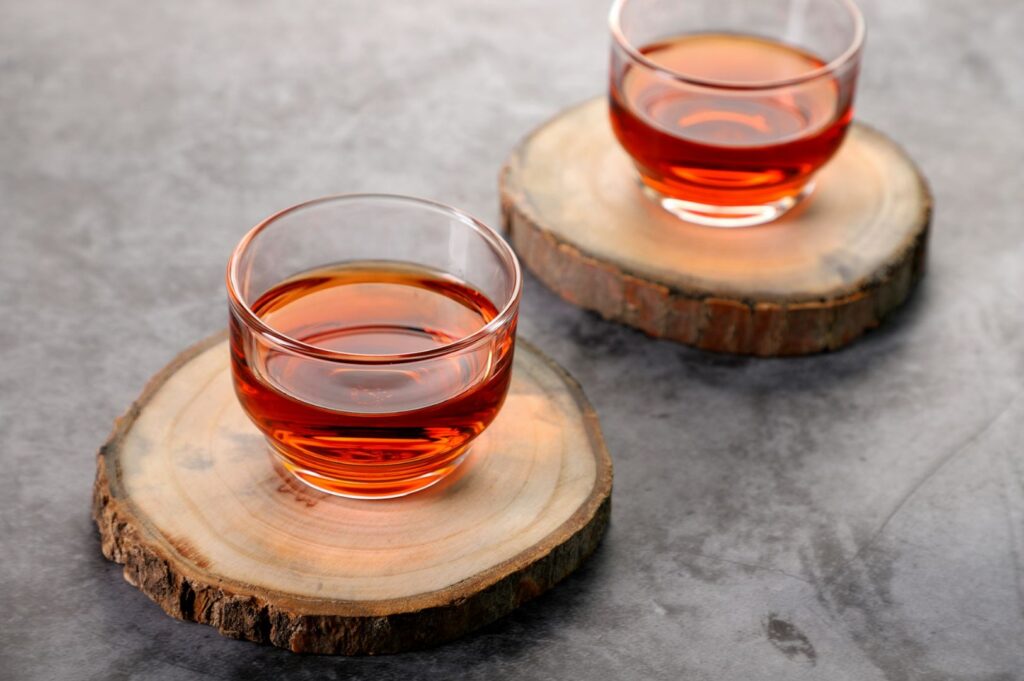 Symmetrical arrangement of two glass cups showcases the deep copper tones of black tea against a textured gray surface, suggesting careful service.