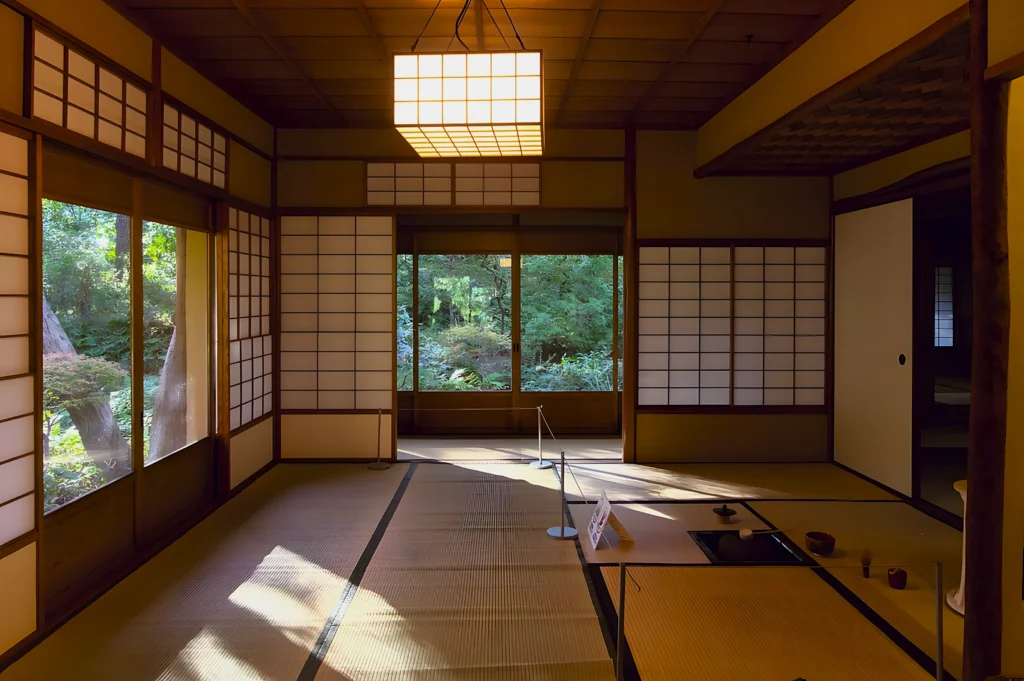 Traditional Japanese tea room with tatami mats and shoji screens, softly illuminated by natural light. A serene garden is visible through the window.